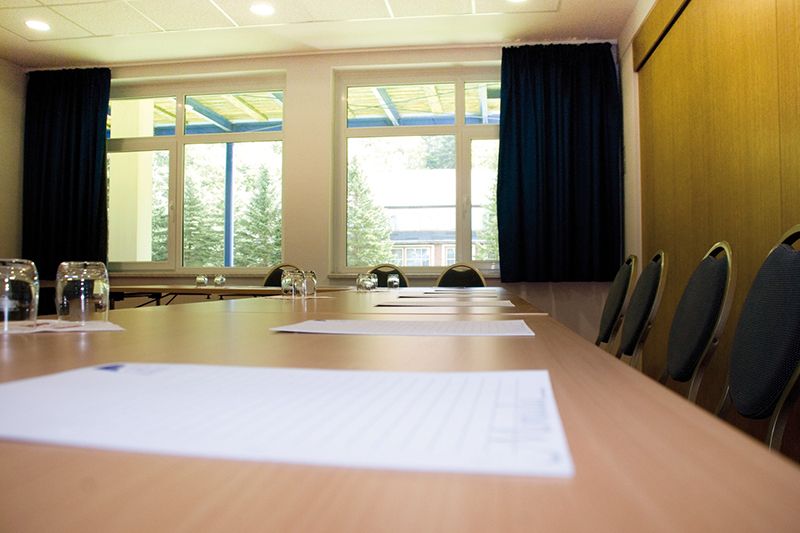 Konferenzraum mit Vorbereitung für ein Treffen Leerer Konferenzraum mit großem Fenster, einem langen Tisch mit Stühlen und Dokumenten darauf.