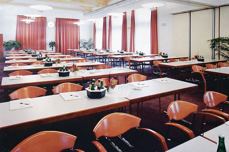 Modern eingerichteter Konferenzraum Konferenzraum mit gedeckten Tischen und roten Stühlen, dekoriert mit Pflanzen und Vorhängen