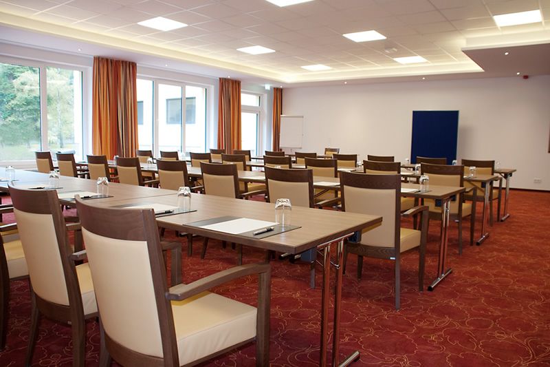 Moderner Konferenzraum bereit für ein Treffen Konferenzraum mit langen Tischen und Stühlen, vorbereitet für ein Meeting mit Gläsern und Schreibmaterialien.