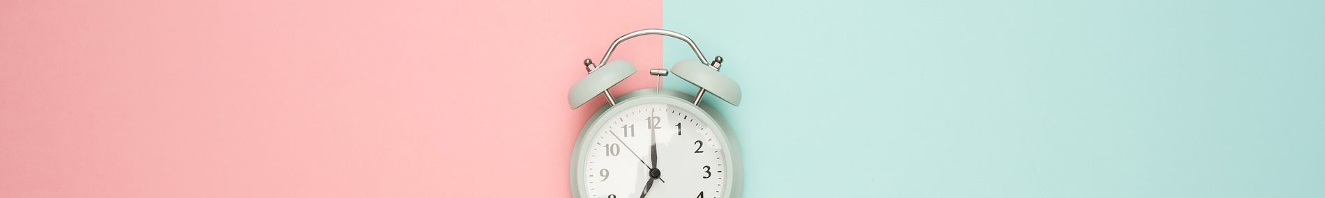 Weißer analoger Wecker auf zweifarbigem Hintergrund in Pink und Türkis